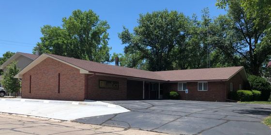 Single-story brick building with a wide driveway and large trees on a sunny day