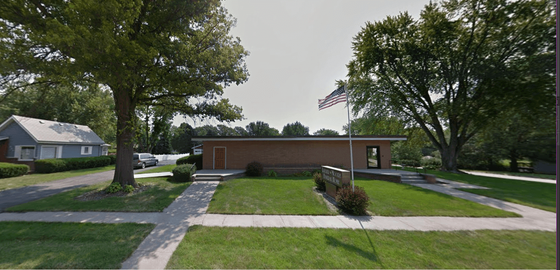 Suburban brick building with a sidewalk, grassy lawn, and trees on a cloudy day