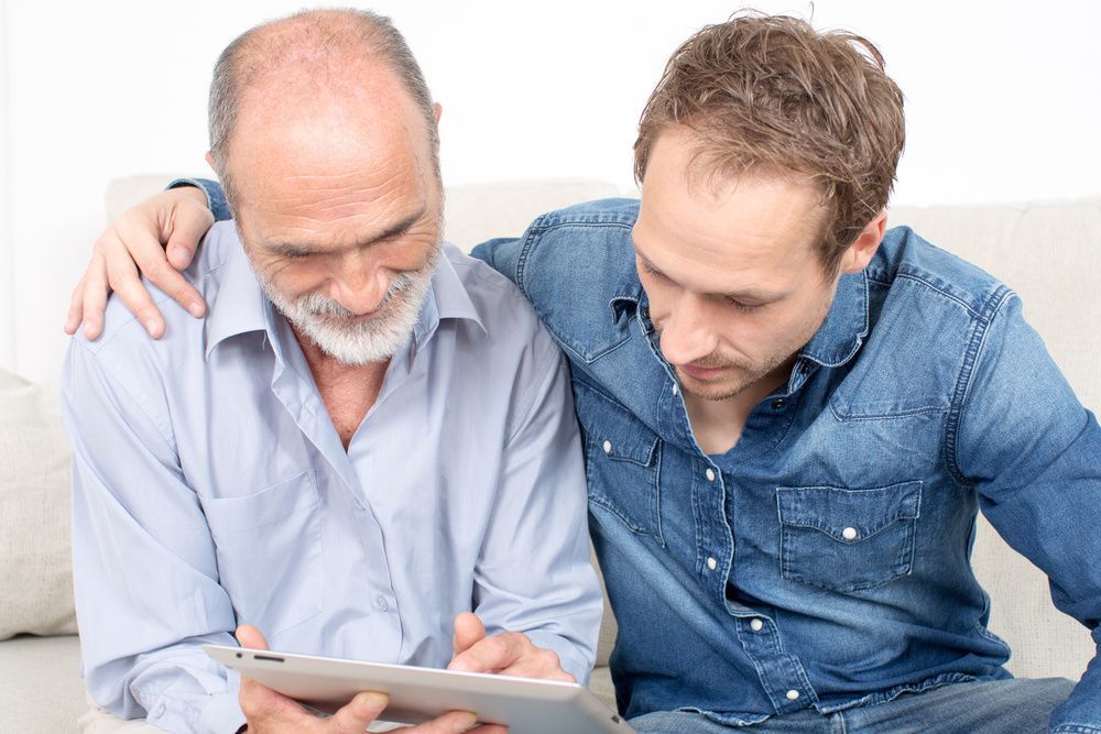 Two people reviewing a tablet together on a couch, one with an arm around the other