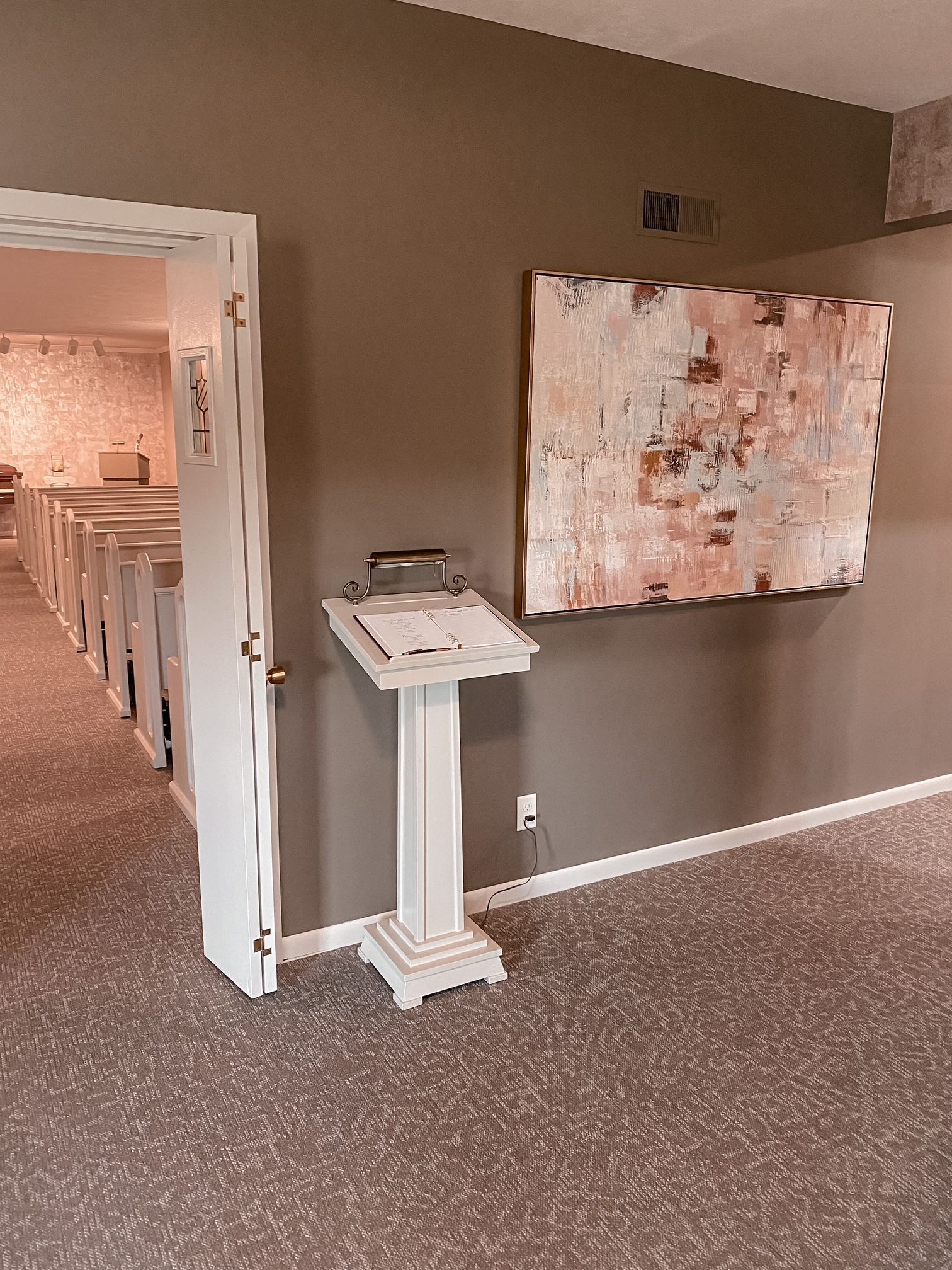 Hallway with an open doorway, a white pedestal, and a large abstract wall painting on a brown wall.