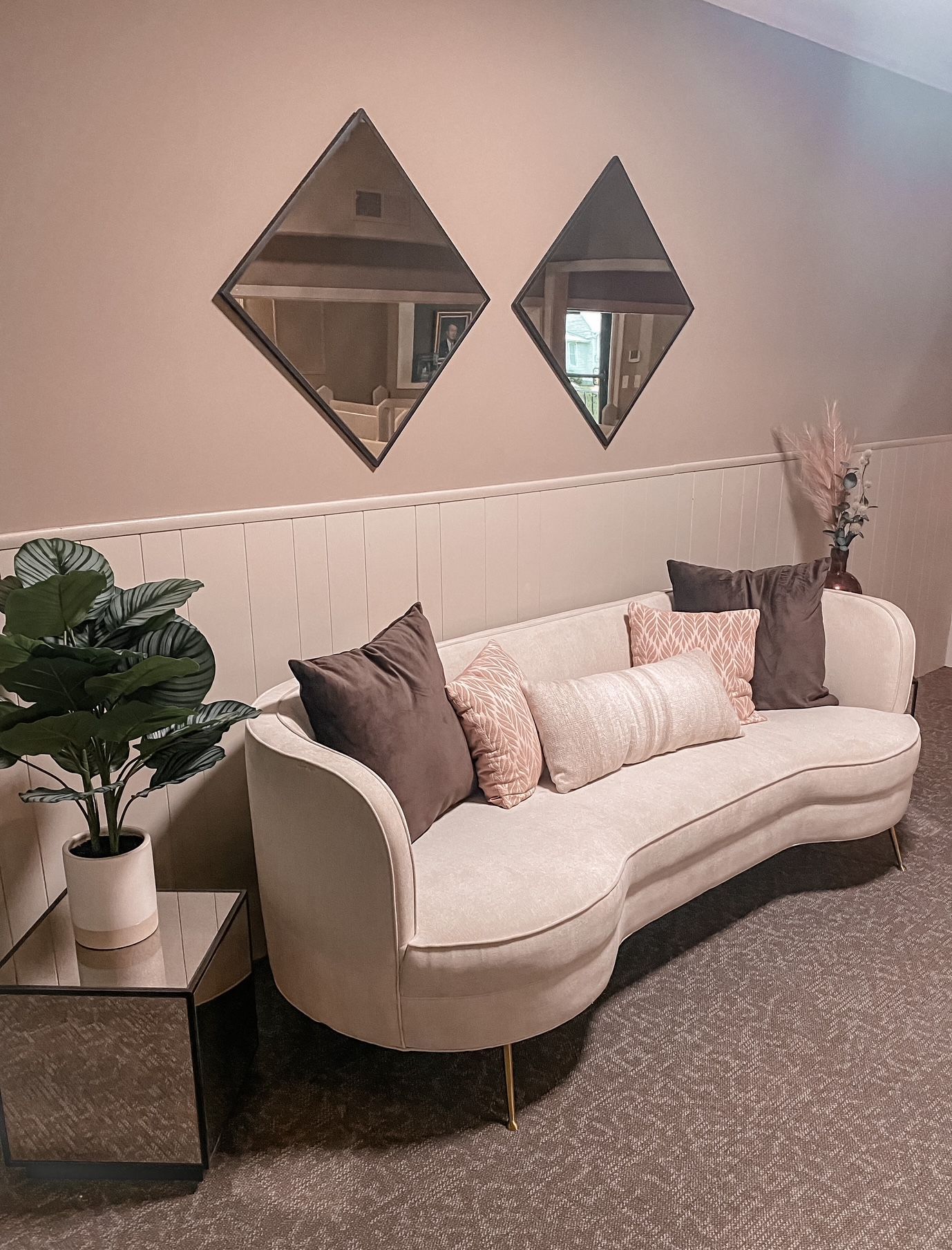 Elegant lounge with cream sofa, patterned carpet, potted plants, and two diamond mirrors on a beige wall