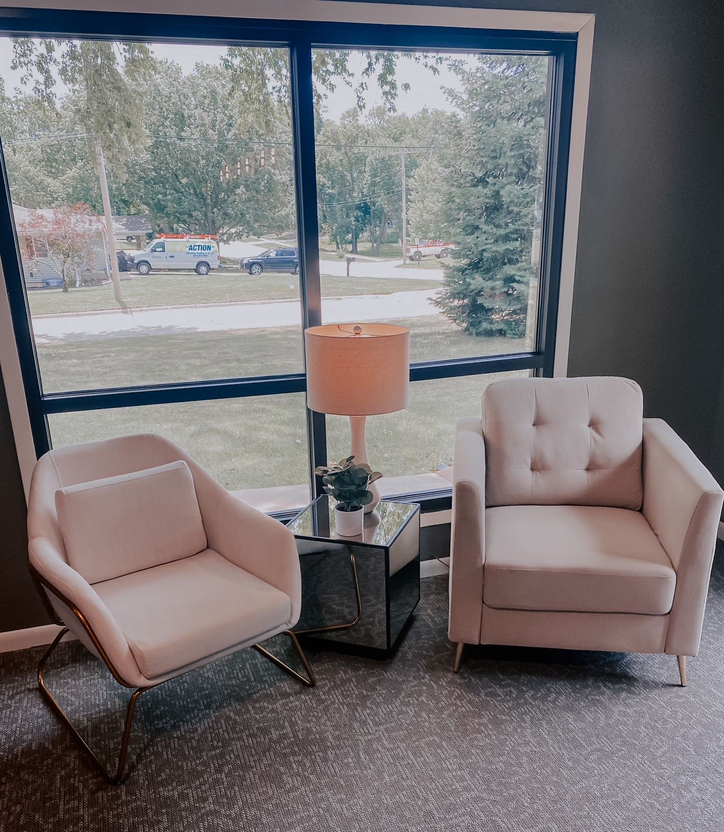 Two blush armchairs beside a lamp in a lobby with a large window view