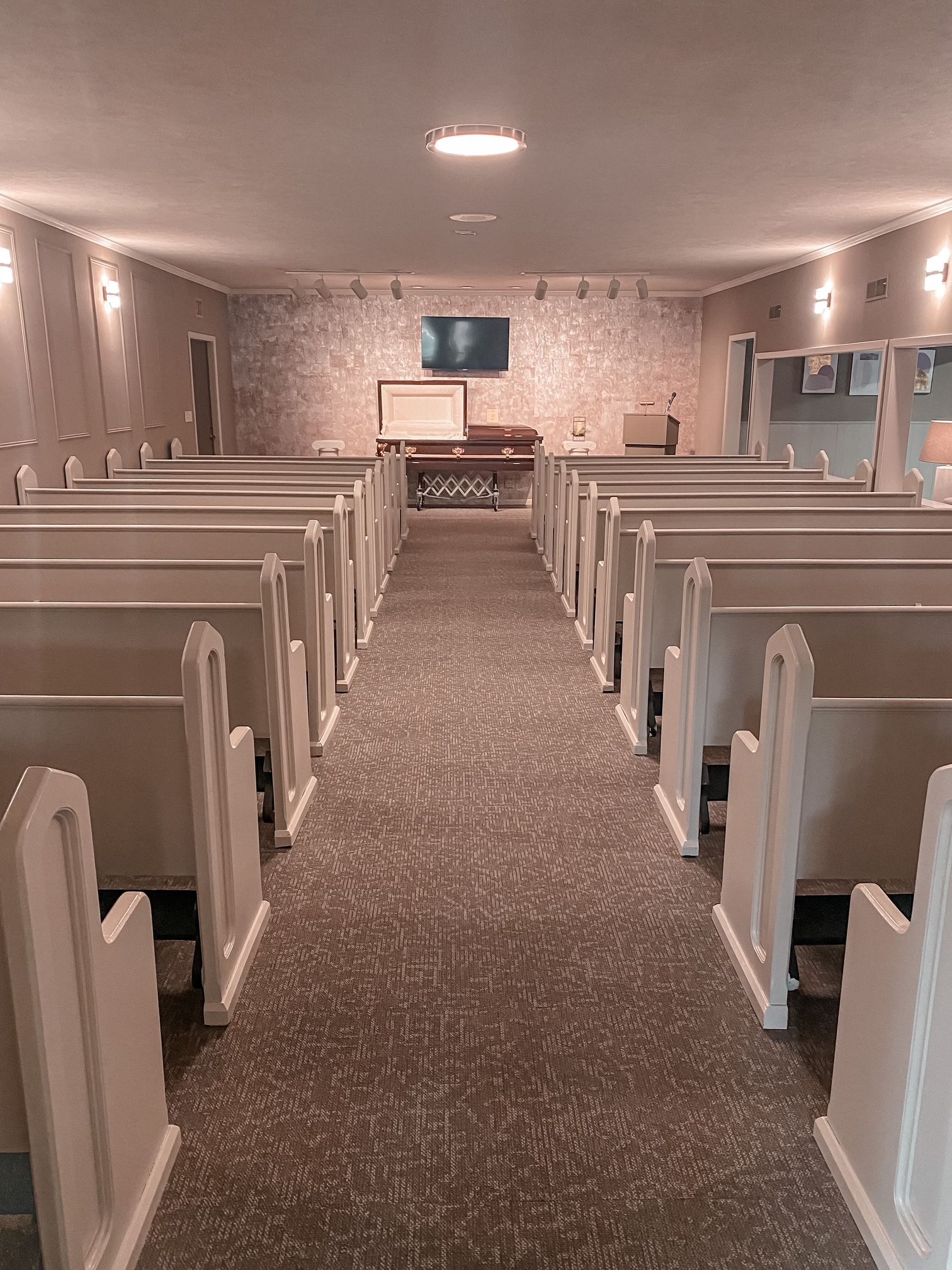 Empty white church chapel with rows of pews facing a pulpit and cross at the front