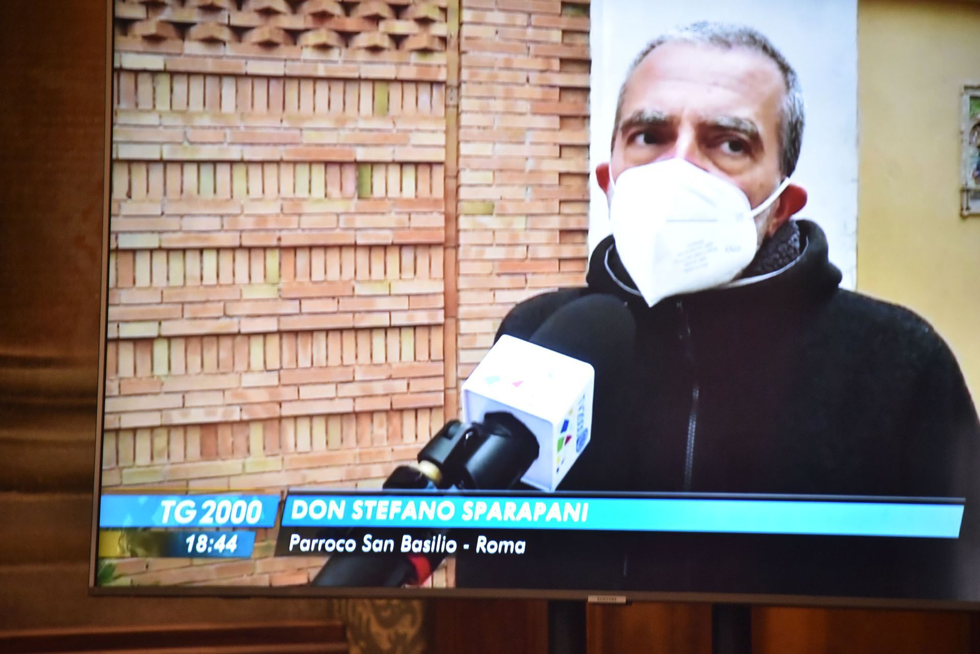 Un uomo che indossa una maschera parla al microfono sullo schermo televisivo