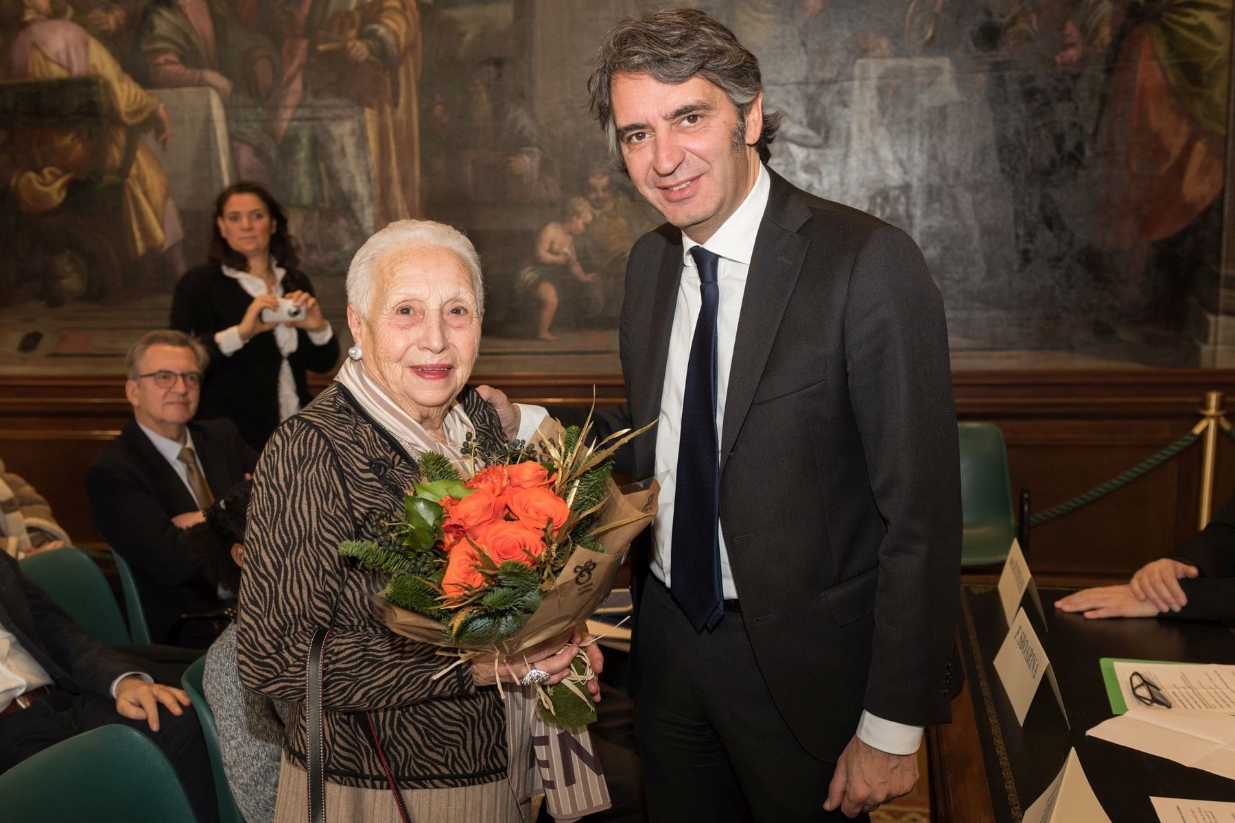 Un uomo in giacca e cravatta è in piedi accanto a una donna che tiene in mano un mazzo di fiori.