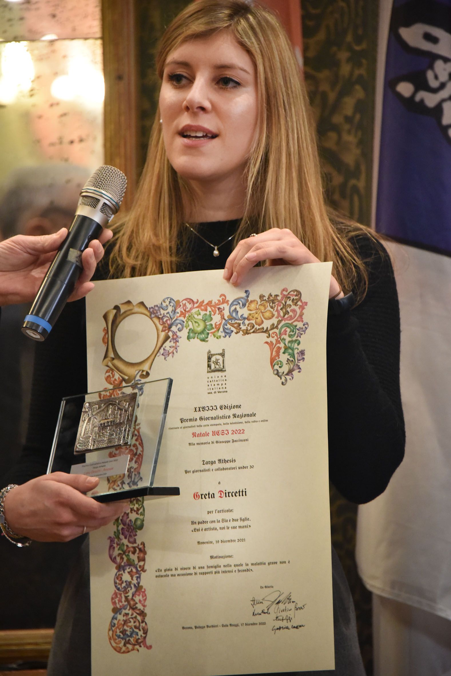 Una donna ha in mano un certificato e un microfono.