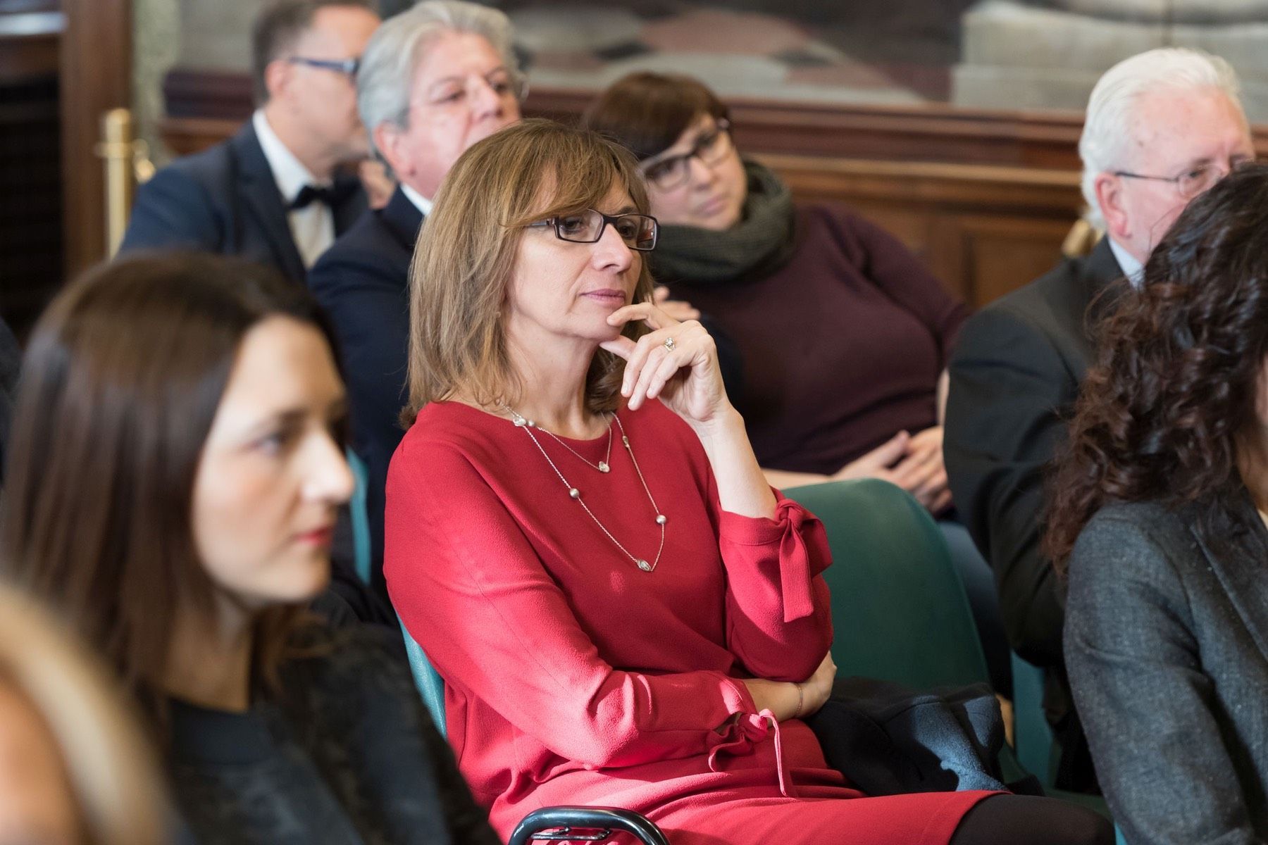 Una donna vestita di rosso è seduta in una fila di persone.