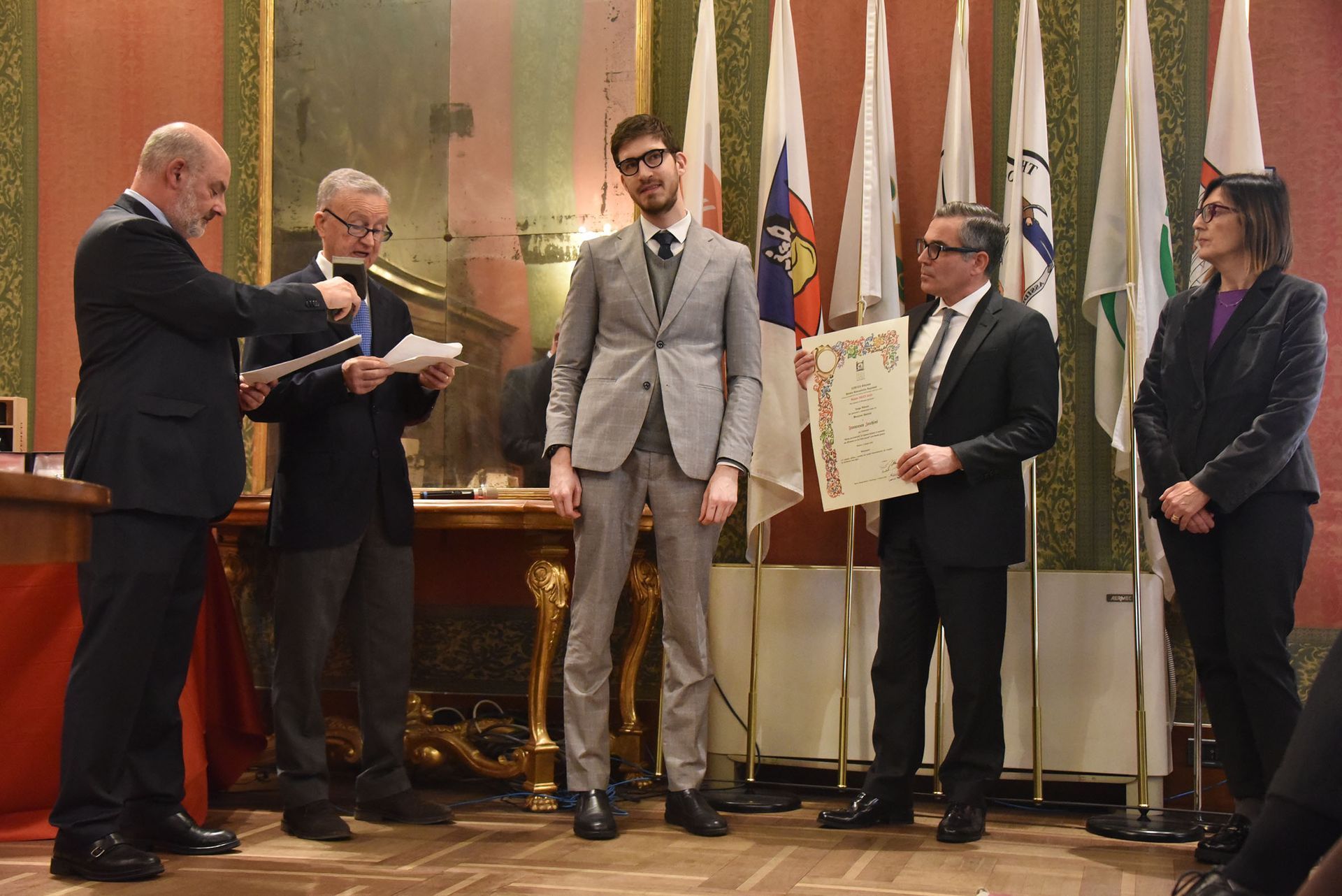 Un uomo in giacca e cravatta è in piedi di fronte a un gruppo di persone in possesso di un certificato.