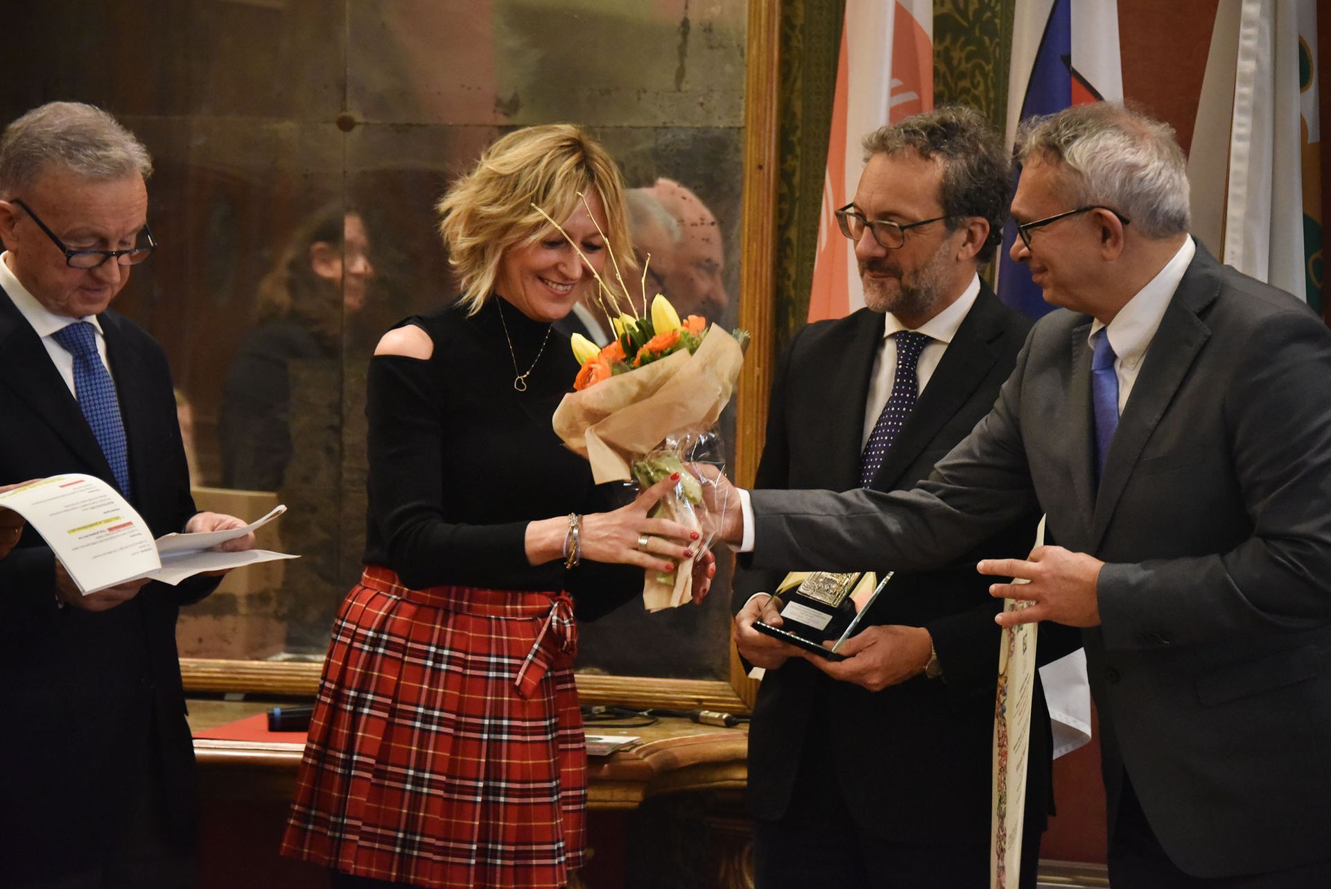 Un gruppo di uomini circonda una donna che tiene in mano un mazzo di fiori.