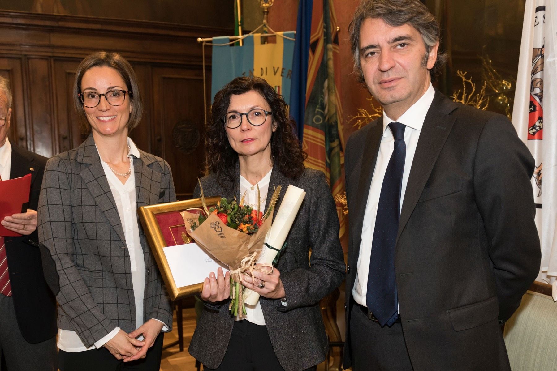Una donna tiene in mano un mazzo di fiori mentre sta in piedi accanto a un uomo in giacca e cravatta.