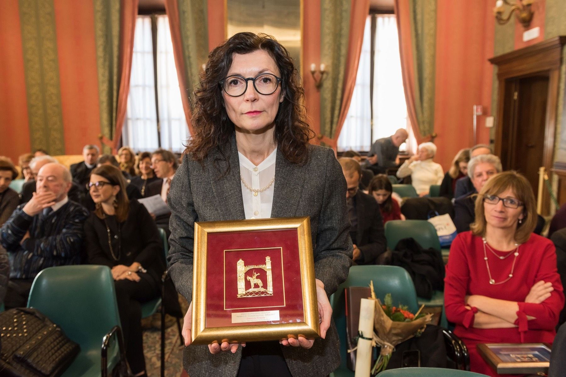 Una donna tiene in mano una foto incorniciata di fronte a una folla di persone.