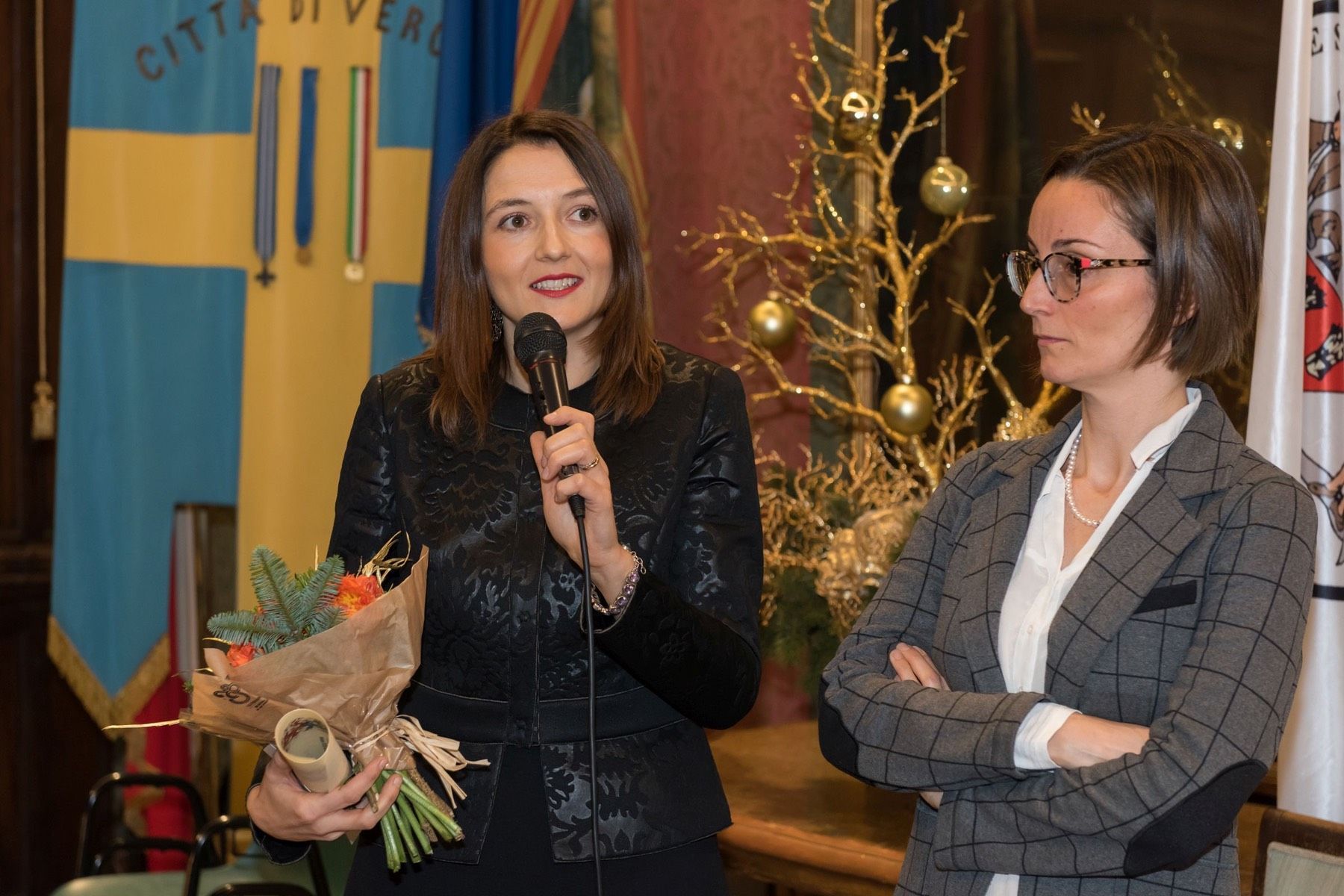 Una donna tiene in mano un mazzo di fiori mentre parla al microfono.