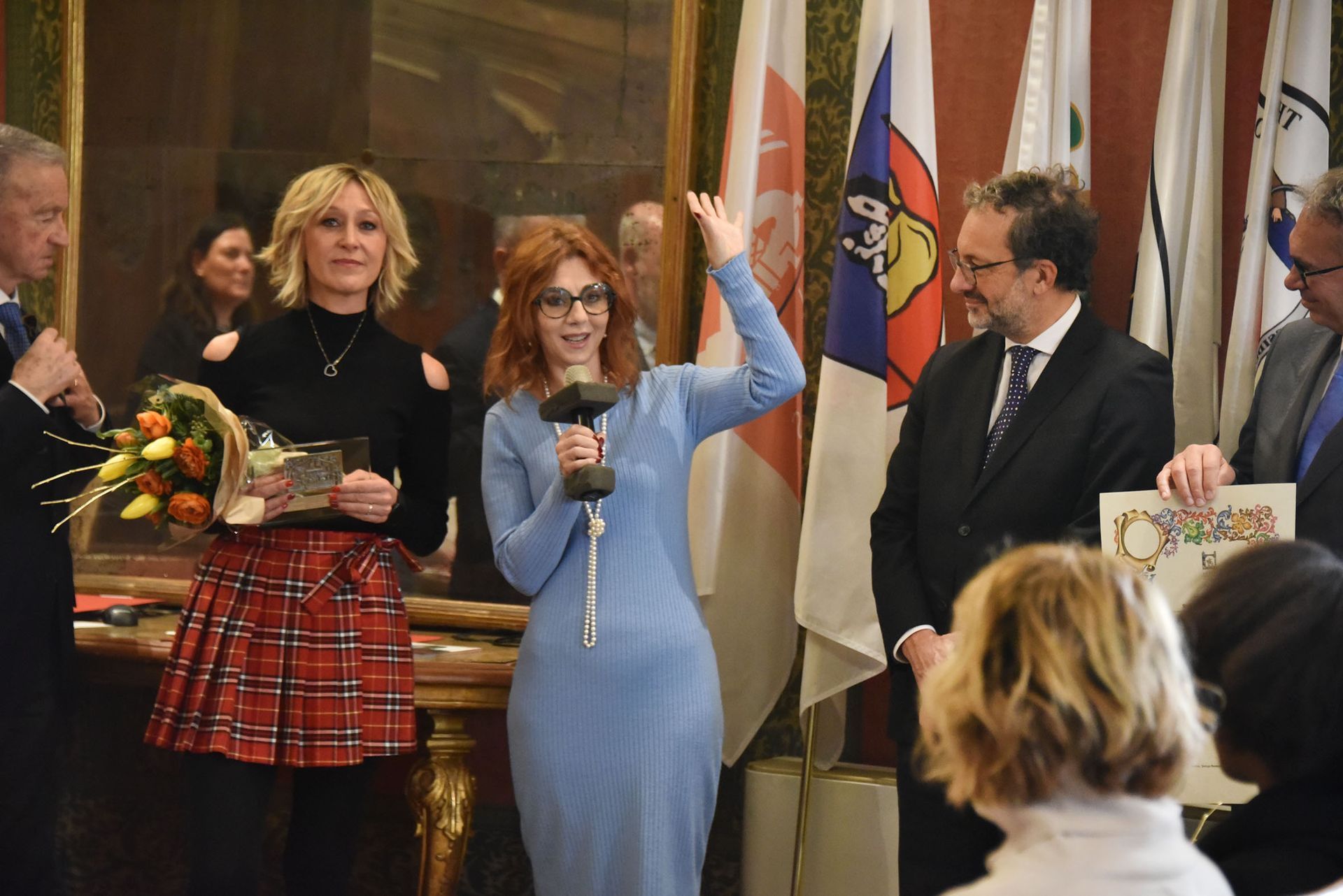 Una donna vestita di blu tiene in mano un trofeo davanti a un gruppo di persone.
