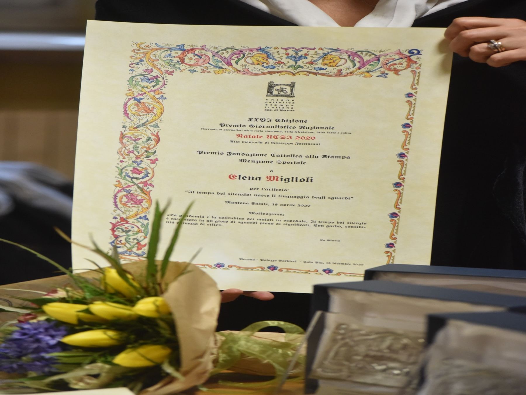 Una donna tiene in mano un certificato davanti a un mazzo di fiori