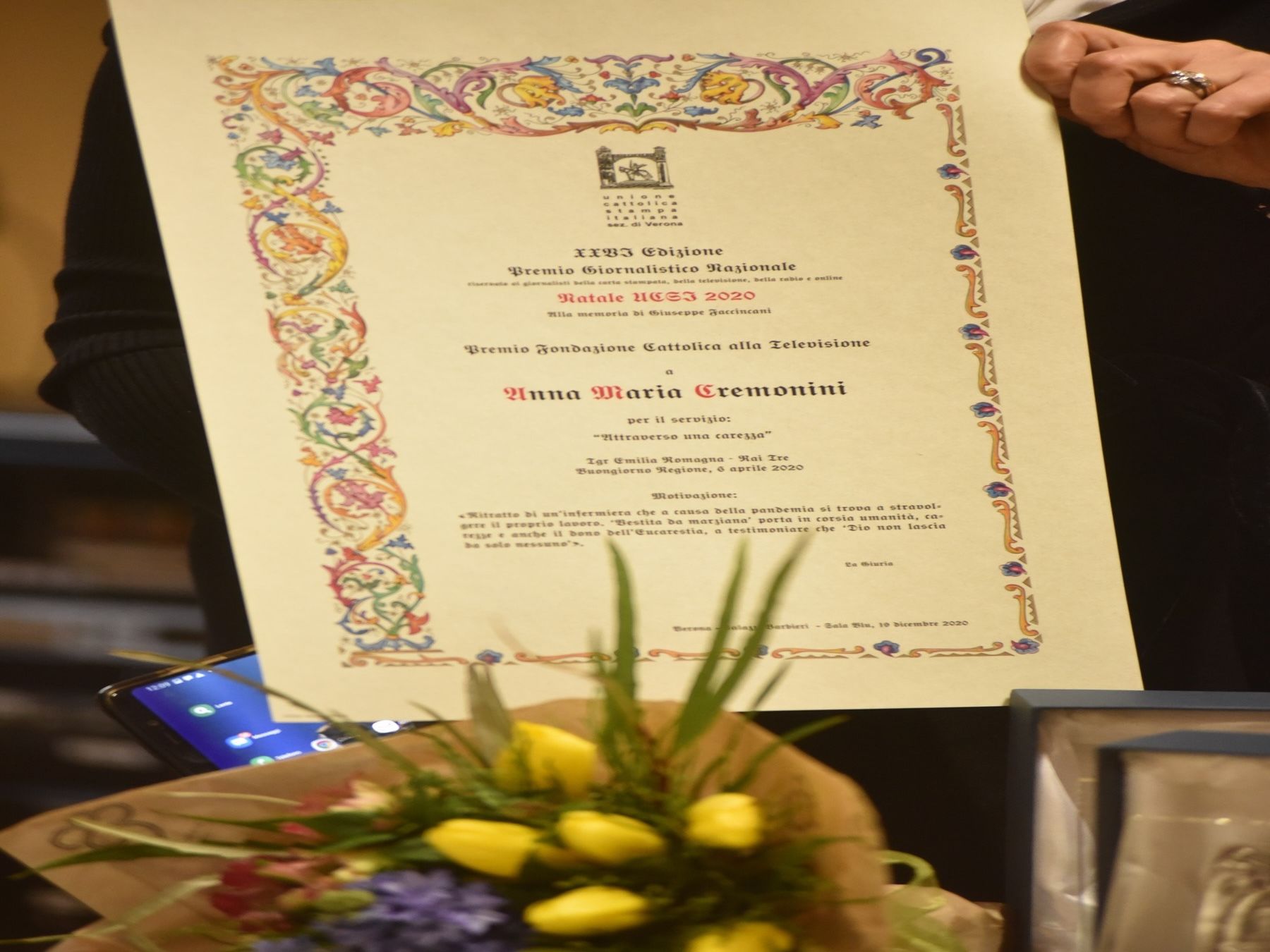Una donna tiene in mano un certificato davanti a un mazzo di fiori