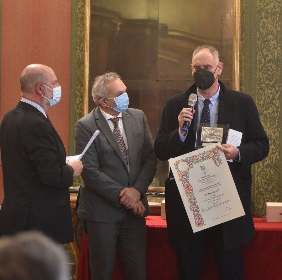 Un uomo che indossa una maschera tiene in mano un certificato e parla al microfono