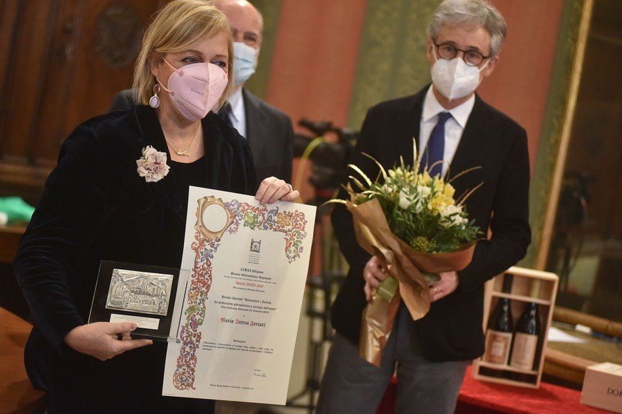 Una donna che indossa una maschera tiene in mano un certificato e un mazzo di fiori.