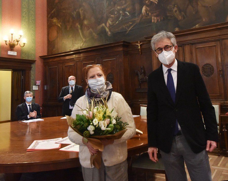 Un uomo e una donna che indossano maschere per il viso sono in piedi uno accanto all'altro con in mano un mazzo di fiori.