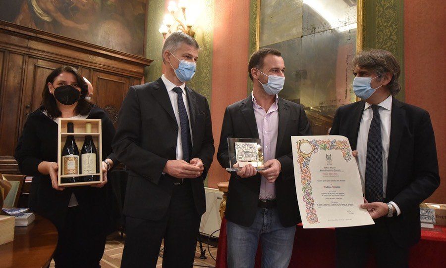 Un gruppo di persone che indossano maschere per il viso tengono in mano bottiglie di vino e un certificato.