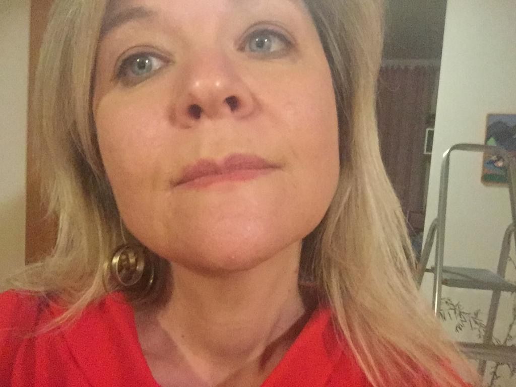 Un primo piano del volto di una donna che indossa una camicia rossa e orecchini.