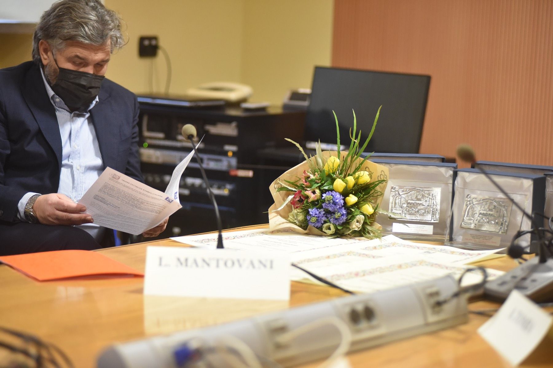 Un uomo che indossa una maschera è seduto a un tavolo con un mazzo di fiori.