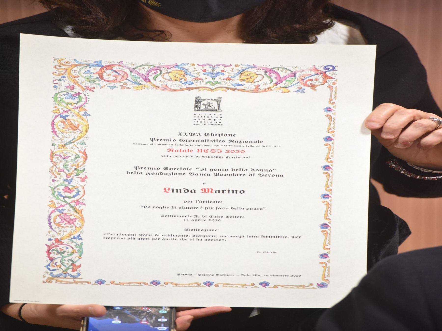Una donna che indossa una maschera ha in mano un certificato e un telefono cellulare.