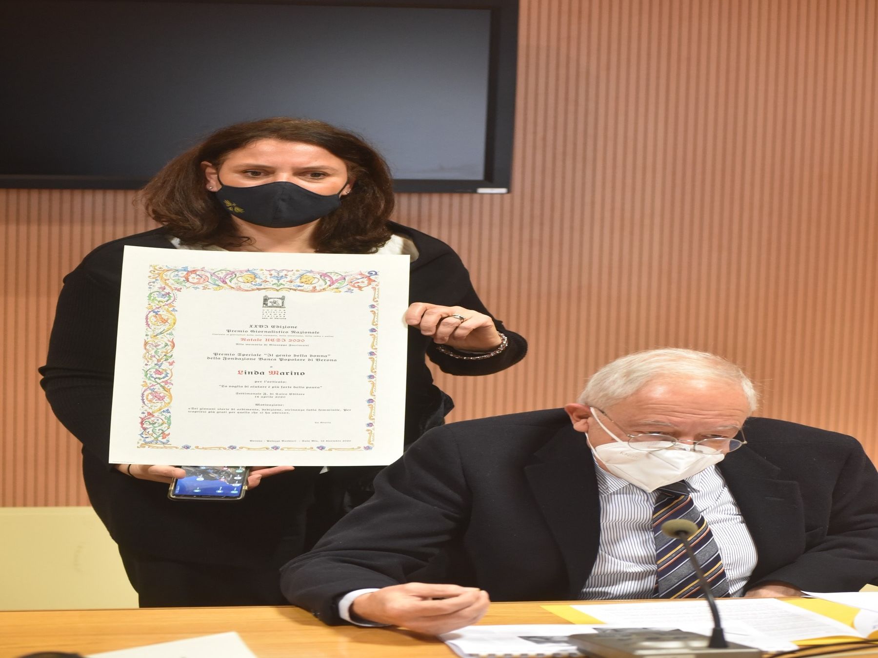 Un uomo e una donna che indossano maschere sono seduti a un tavolo con in mano un certificato.