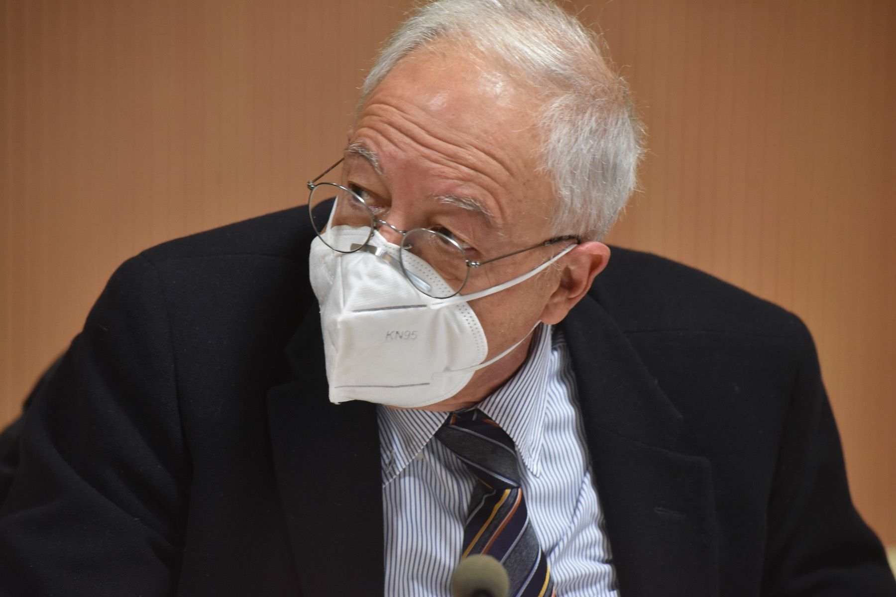Un uomo in giacca e cravatta indossa una maschera.