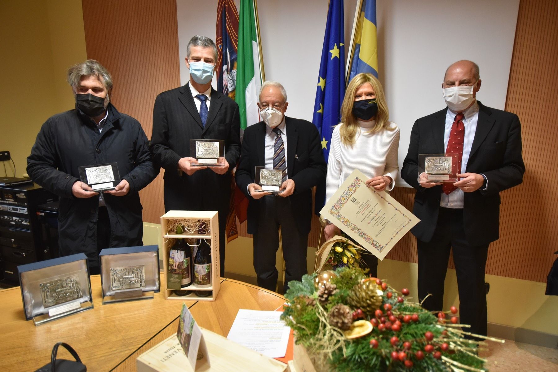 Un gruppo di persone che indossano maschere per il viso sono in piedi attorno a un tavolo con in mano dei premi.