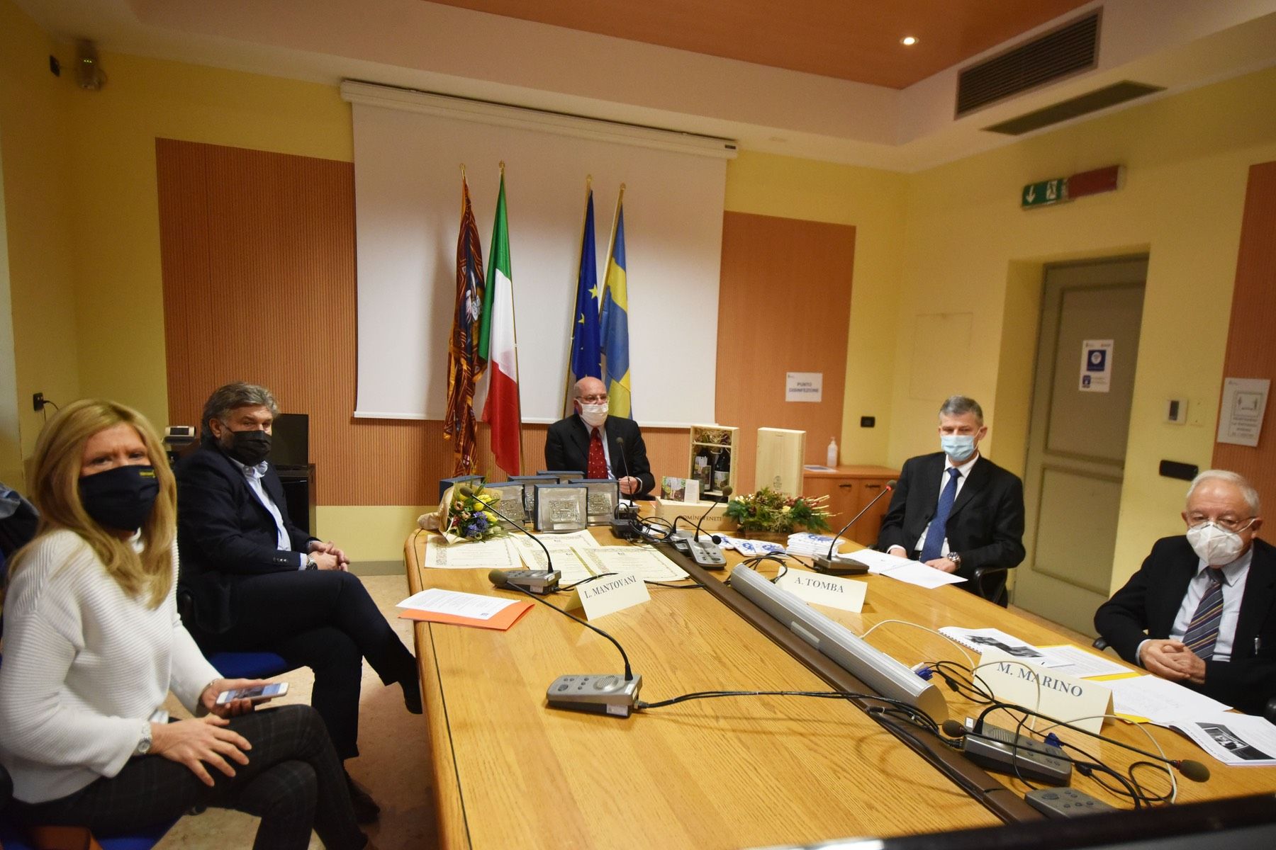 Un gruppo di persone che indossano maschere per il viso sono sedute attorno a un tavolo da conferenza.