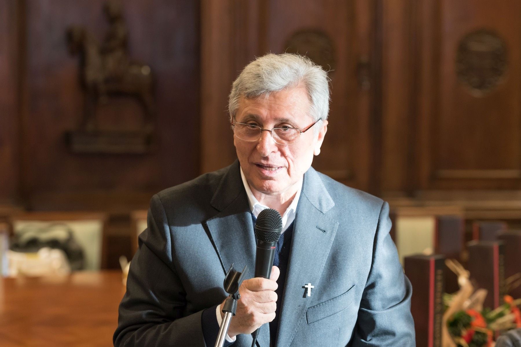 Un uomo in giacca e cravatta tiene in mano un microfono in una stanza.