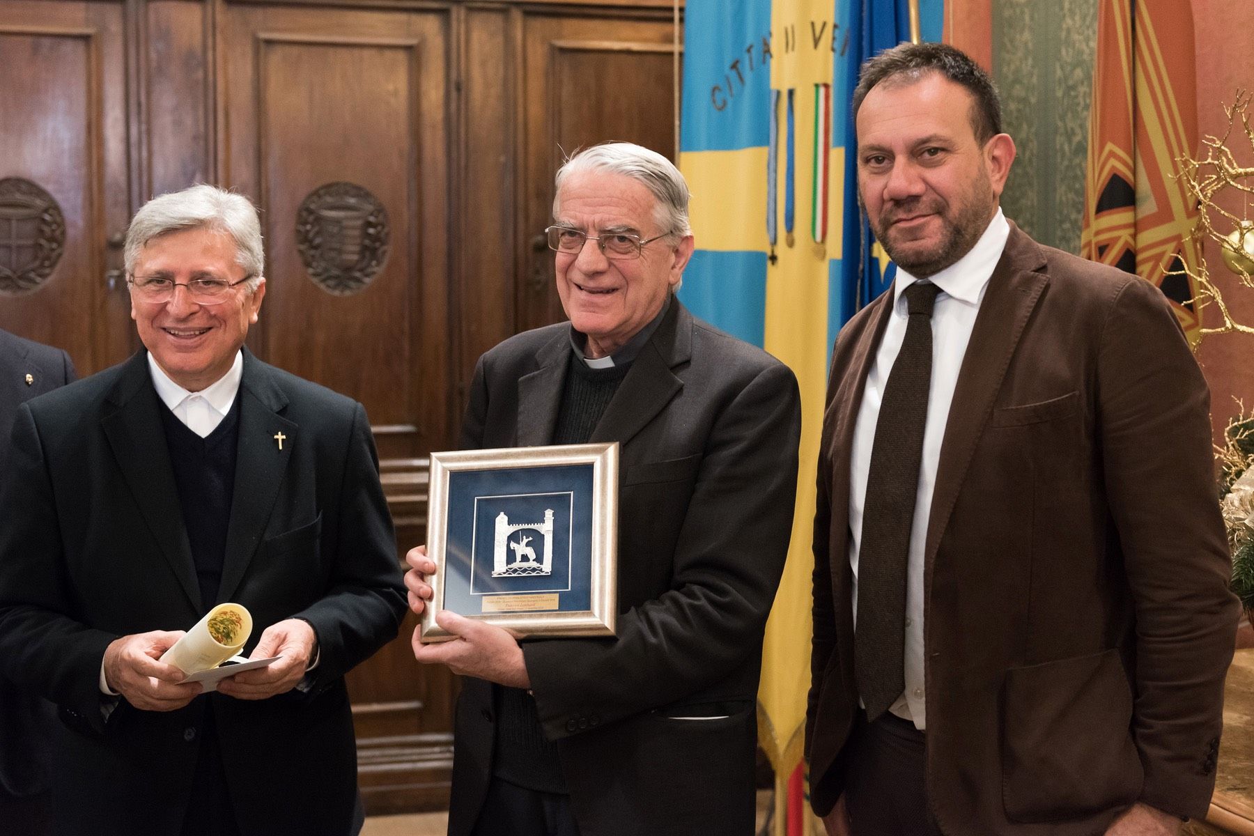 Tre uomini sono in piedi uno accanto all'altro e uno di loro tiene in mano una foto incorniciata.