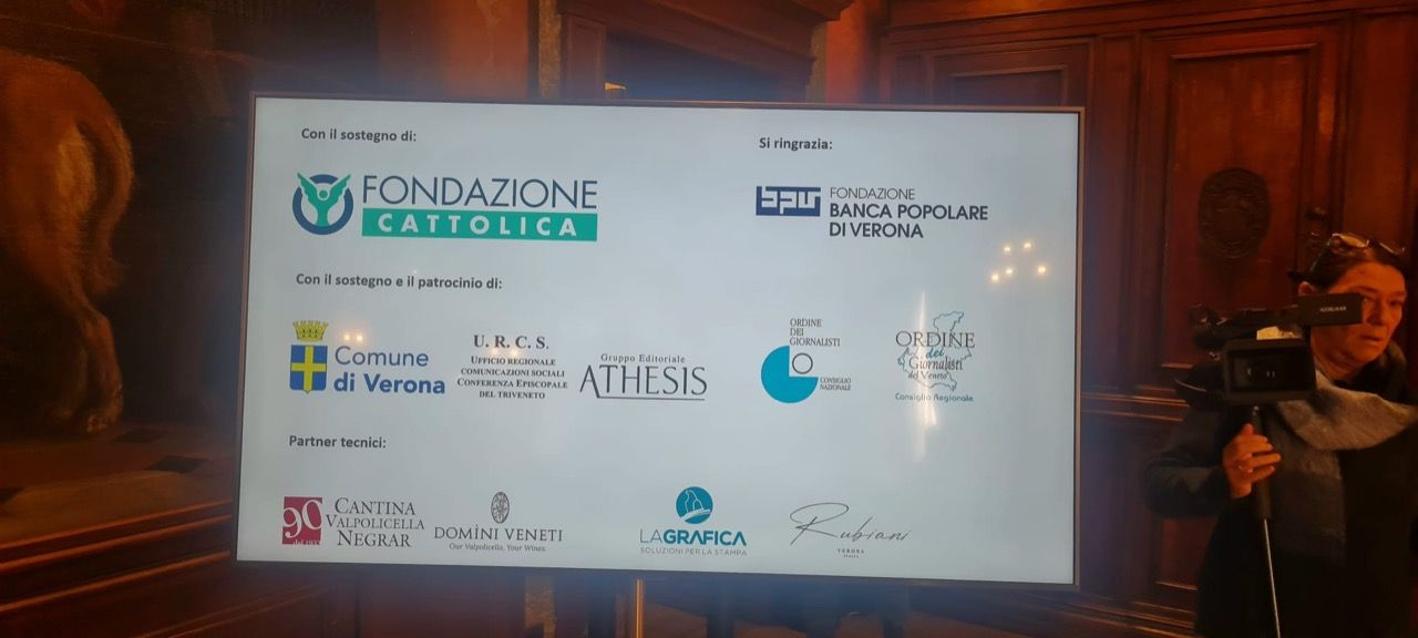 Un uomo è in piedi davanti a un grande schermo con dei loghi sopra.