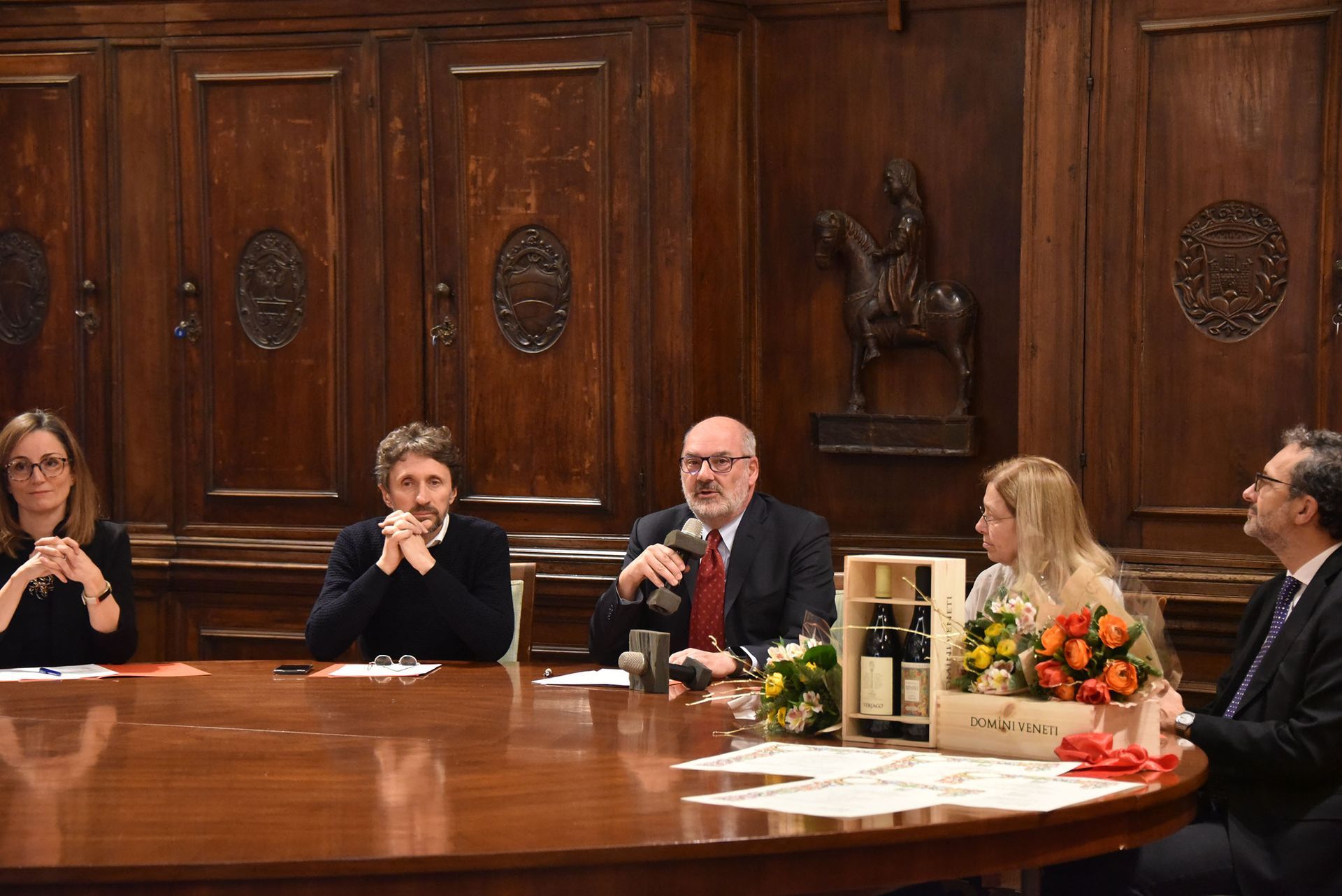 Un gruppo di persone è seduto attorno a un tavolo e parla ai microfoni.