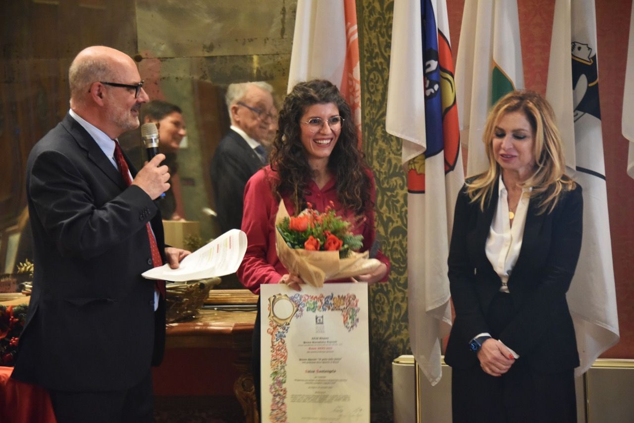Un uomo consegna un certificato a una donna mentre una donna tiene in mano un mazzo di fiori.