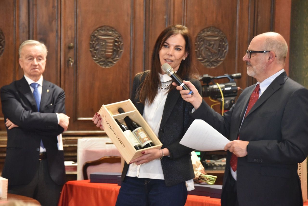 Una donna tiene in mano una scatola di vino mentre parla al microfono.