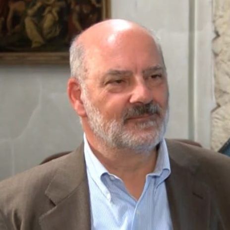 Un uomo calvo con una camicia a quadri sorride alla telecamera.