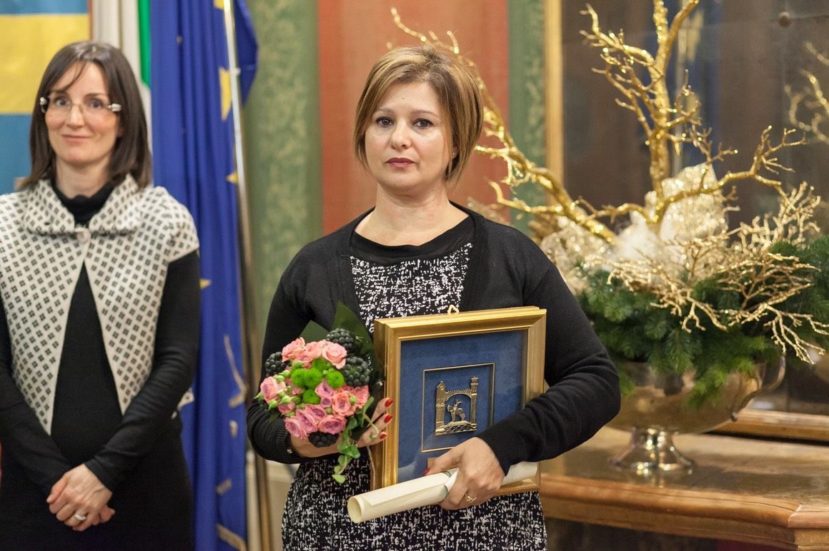 Una donna tiene in mano un quadro incorniciato e un mazzo di fiori.