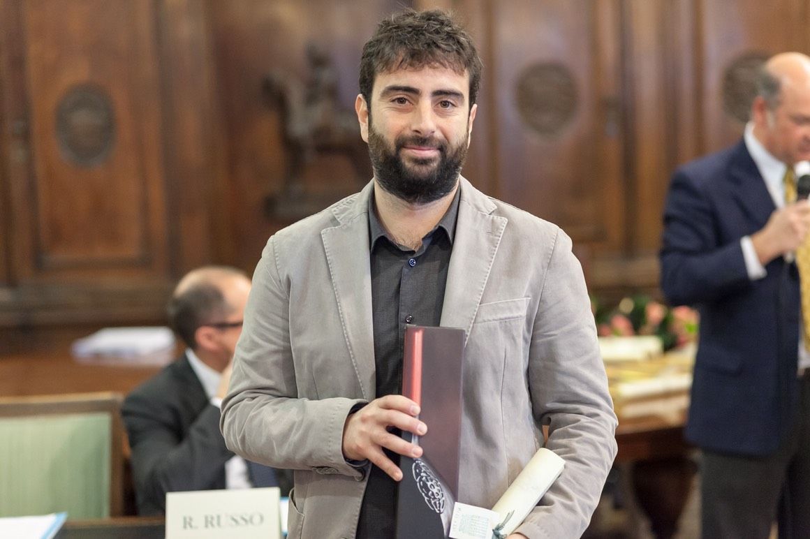 Un uomo con la barba tiene in mano un libro in una stanza.