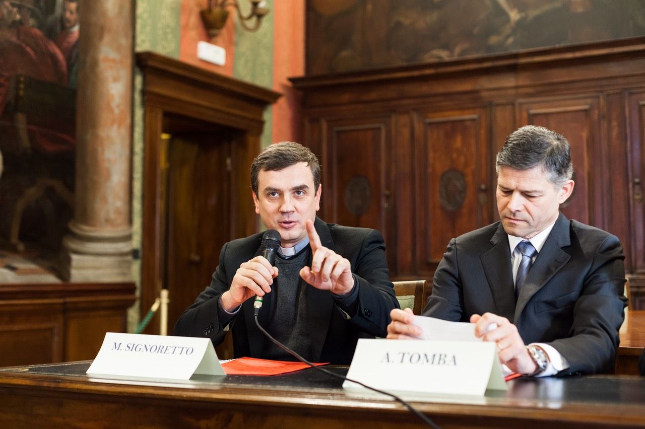 Due uomini sono seduti a un tavolo e parlano ai microfoni.