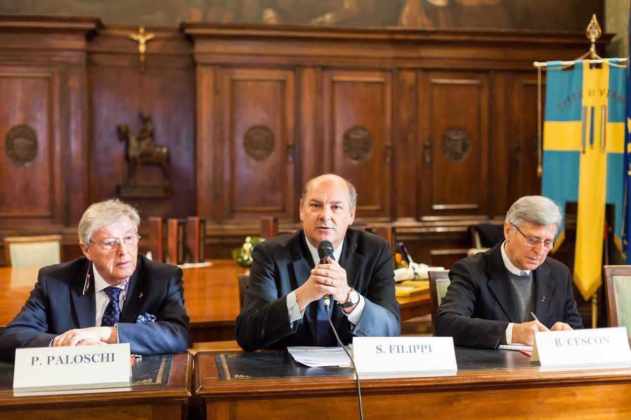 Tre uomini sono seduti a un tavolo e parlano ai microfoni.
