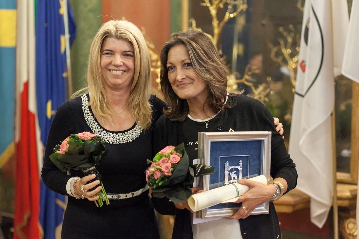 Due donne sono in piedi una accanto all'altra con fiori e un certificato.