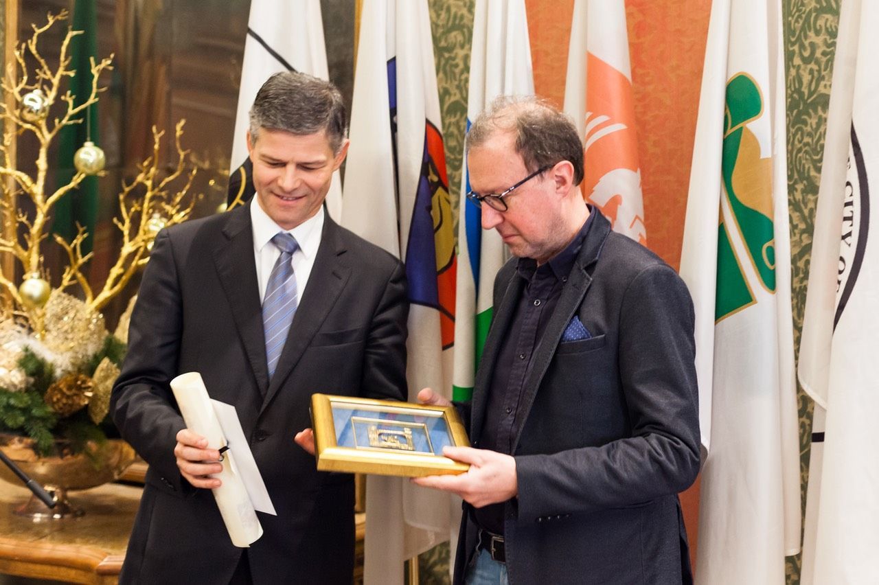 Due uomini in giacca e cravatta sono in piedi uno accanto all'altro con in mano una foto incorniciata.