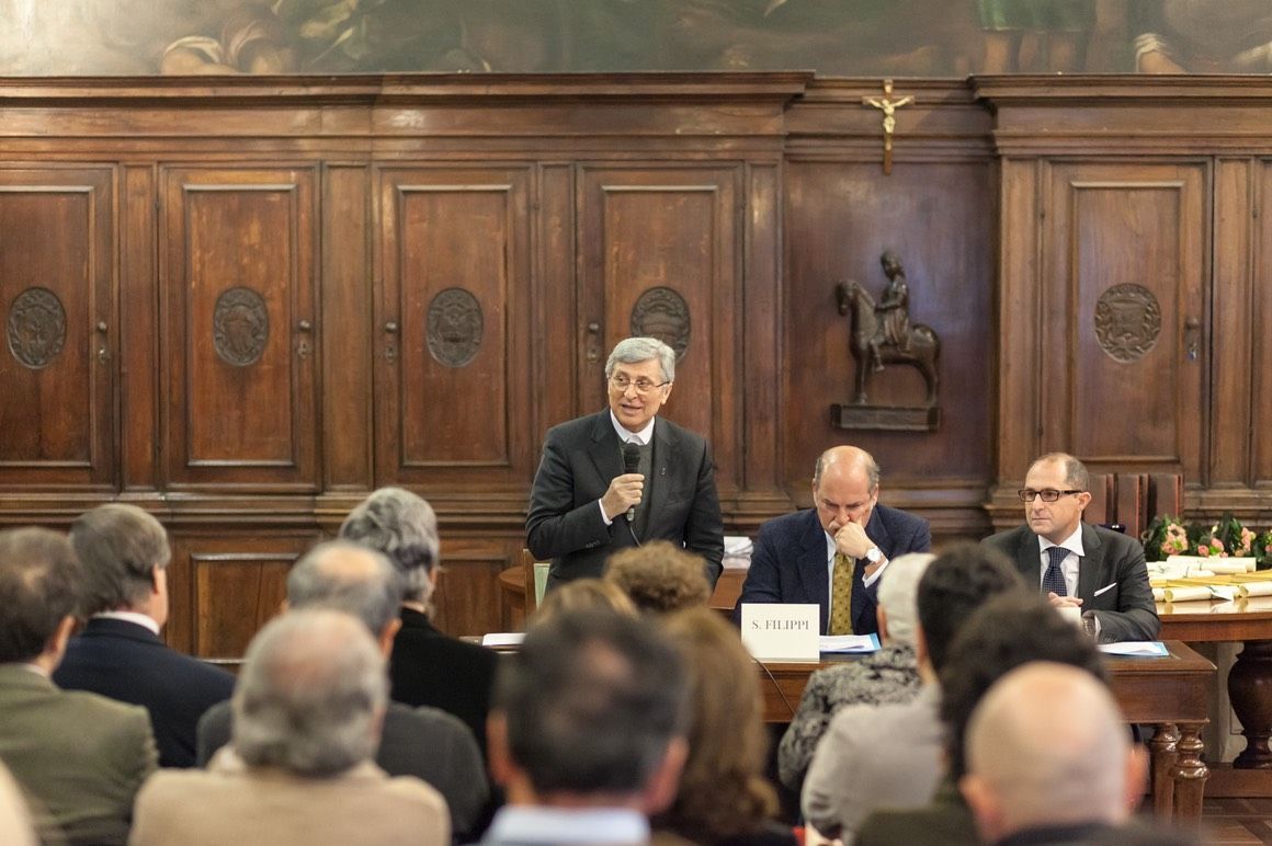 Un uomo parla al microfono di fronte a un gruppo di persone in una stanza.