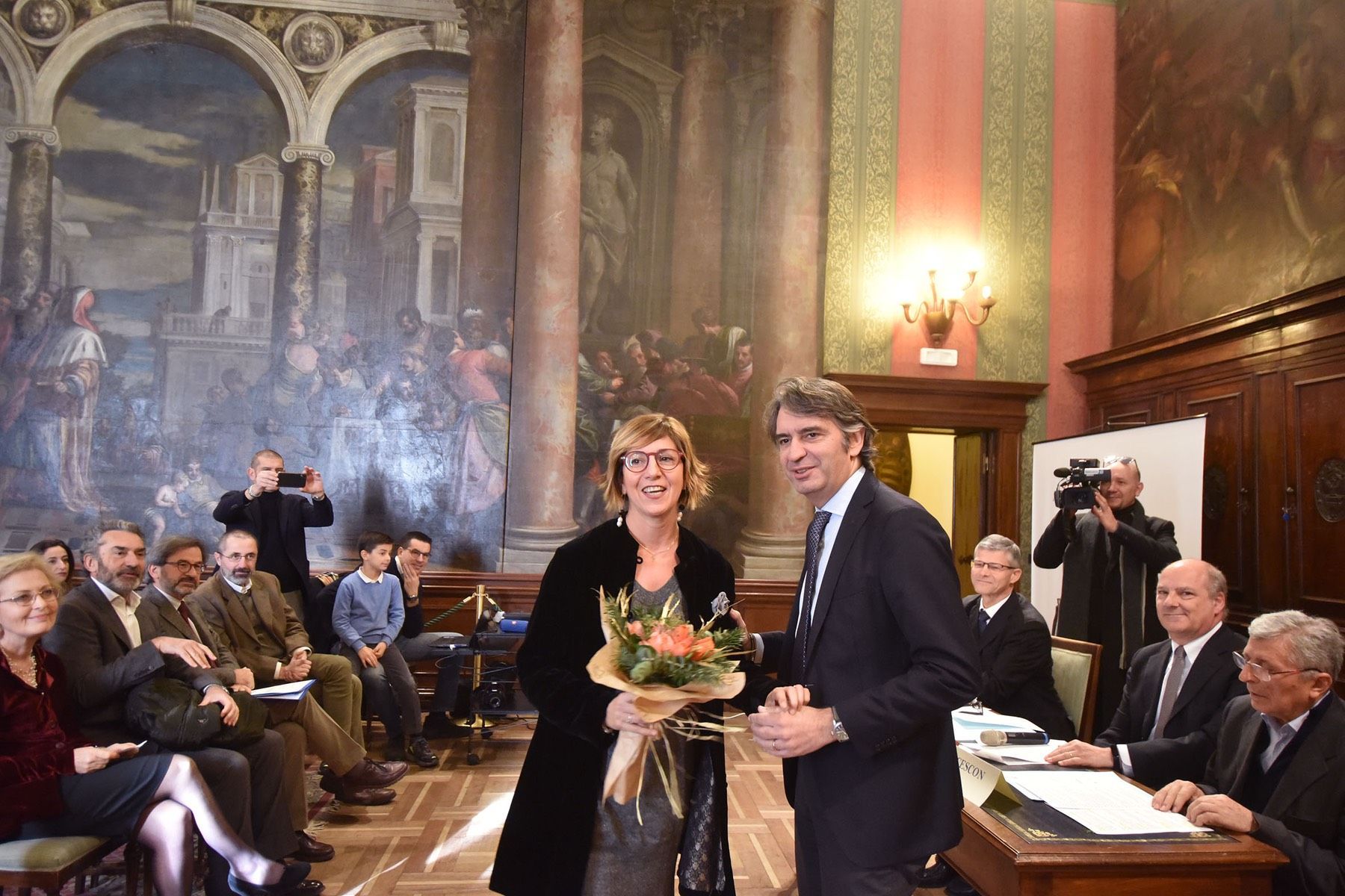 Un uomo in giacca e cravatta stringe la mano a una donna che tiene in mano un mazzo di fiori.