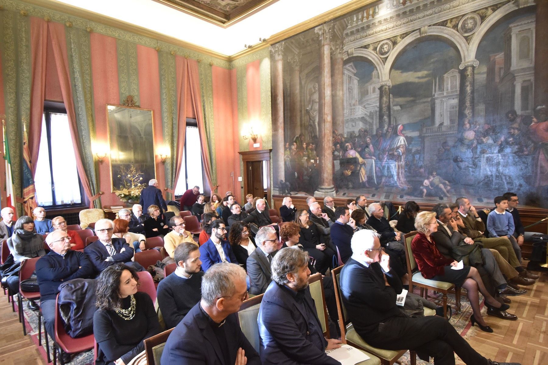 Un gruppo di persone è seduto in una stanza con un grande dipinto sul muro.