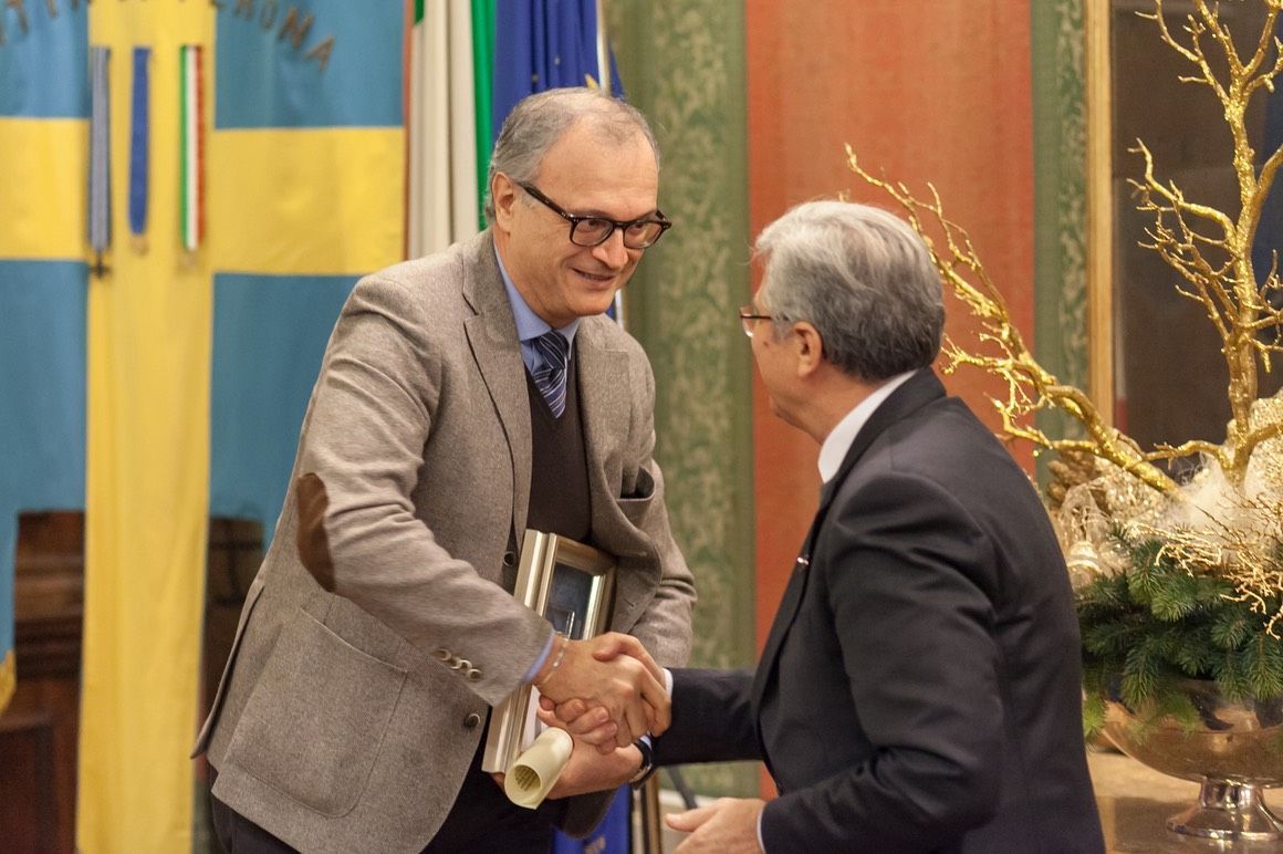 Due uomini si stringono la mano davanti a una bandiera.
