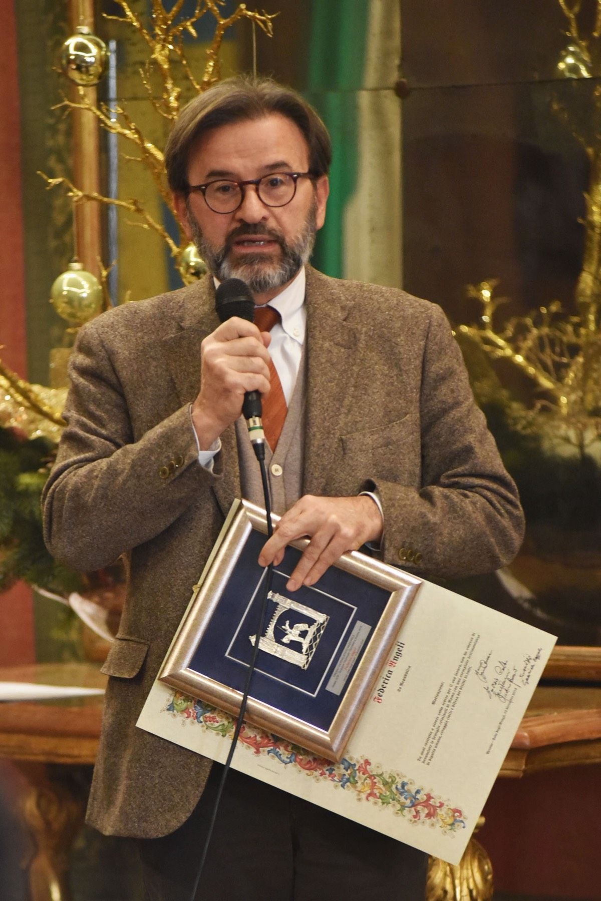 Un uomo in giacca e cravatta tiene in mano un certificato e un microfono.
