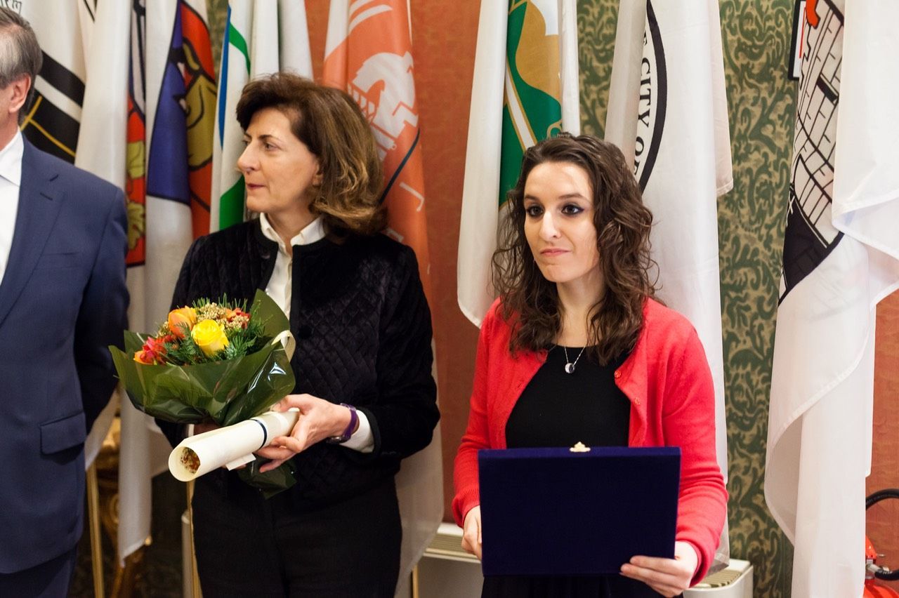 Una donna con una giacca rossa tiene in mano un diploma