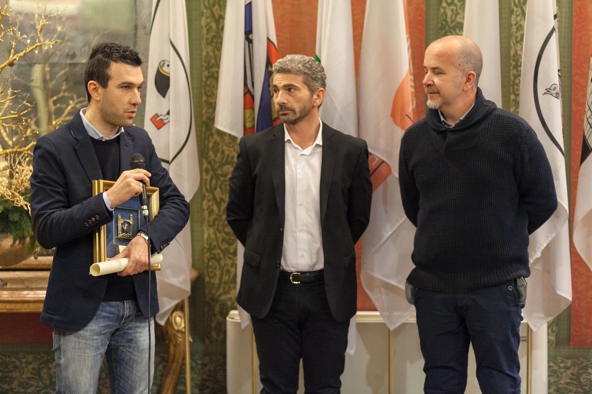 Tre uomini sono in piedi uno accanto all'altro davanti alle bandiere.